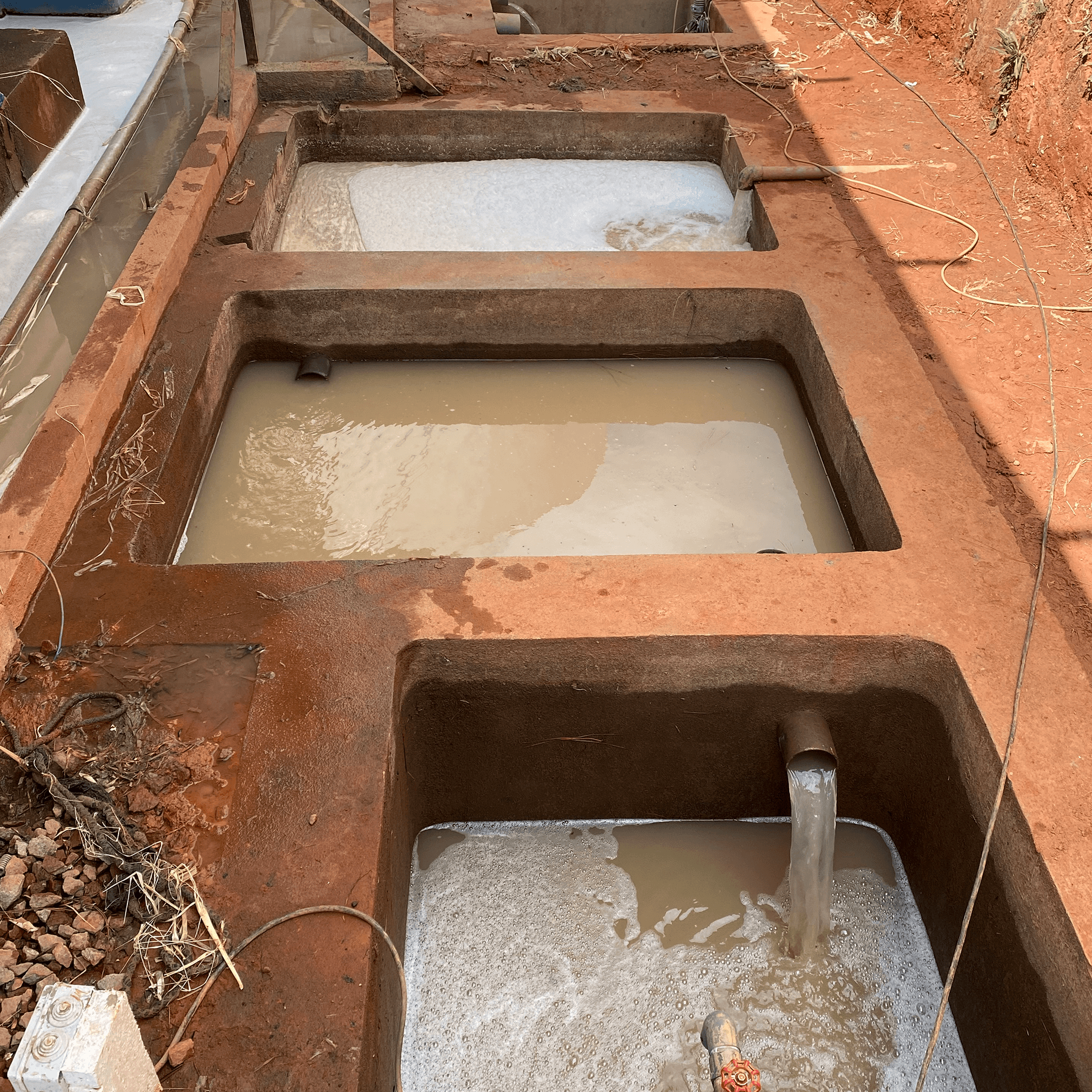 Gros plan sur un bassin recevant les eaux usees brutes avec pompes submersibles et canalisations d'arrivee, illustrant la premiere etape de traitement.