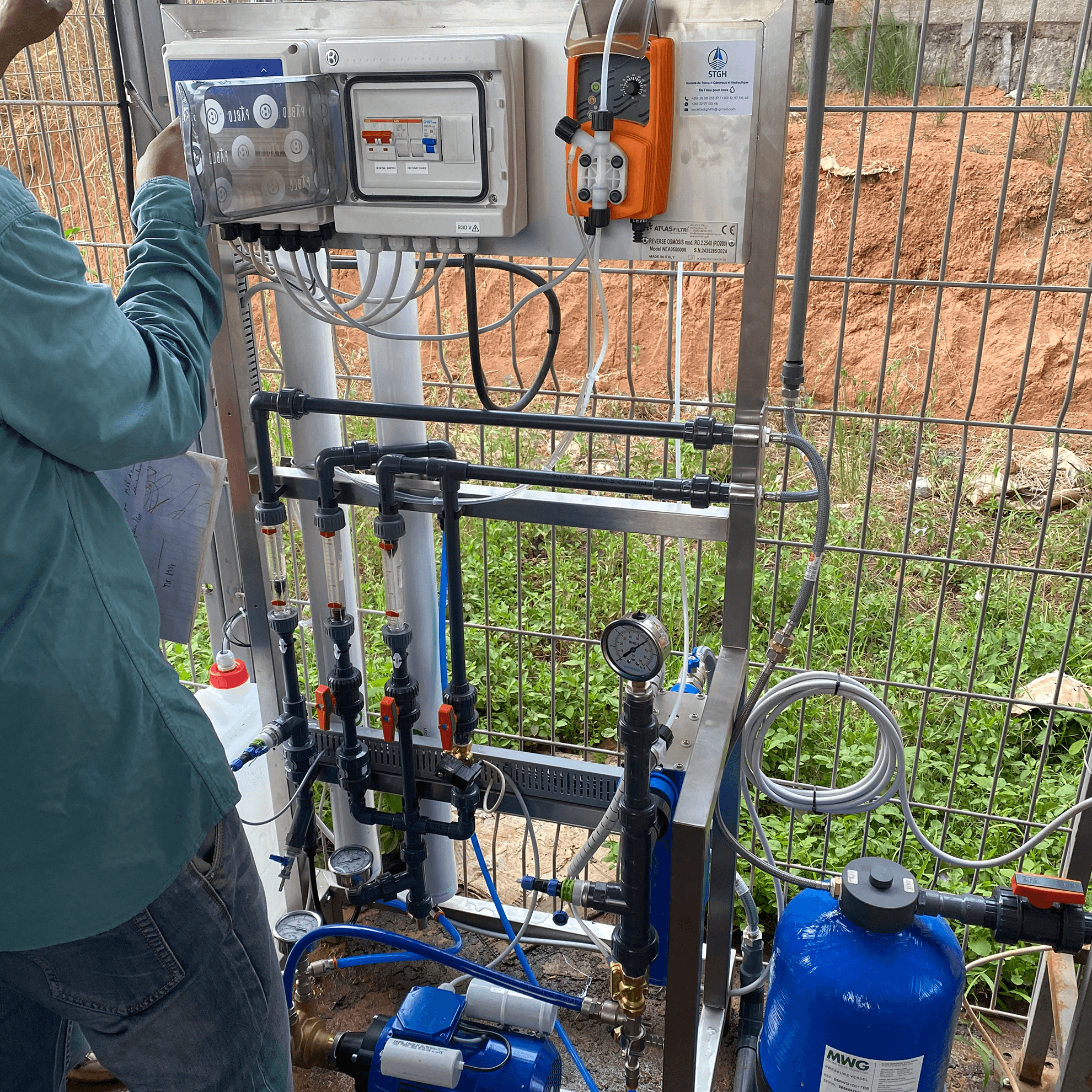 Technicien procedant aux reglages d'un systeme d'osmose inverse avec manometres, pompes et modules de filtration.